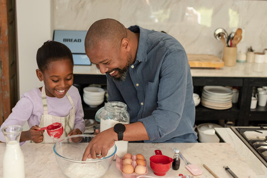 African American father and daughter measuring flour with red cup into glass mixing bowl in kitchen
