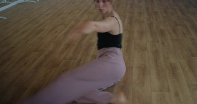 Girl in black top performs smooth movement while dancing contemporary parter on studio floor. Woman moves and dances with arms and body in free contemporary dance sitting