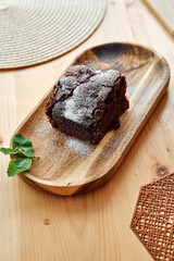 Delicious chocolate cake with powdered sugar on wooden tray with mint garnish
