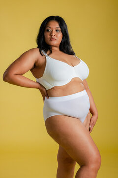 Asian woman posing on yellow studio backdrop wearing white underwire bra and high-waisted briefs