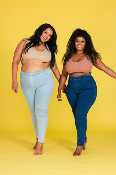 African American female friends walking barefoot on yellow set wearing crop tops and fitted bottoms