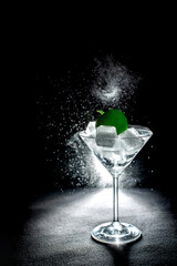 Fresh cocktail with green apple and ice cubes in a martini glass on black background
