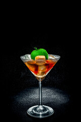 Fresh cocktail with green apple and ice cubes in a martini glass on black background
