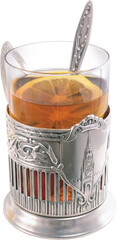 A glass of amber colored tea with a lemon slice and a decorative silver spoon in an ornate antique metal holder with kremlin imagery isolated on transparent background