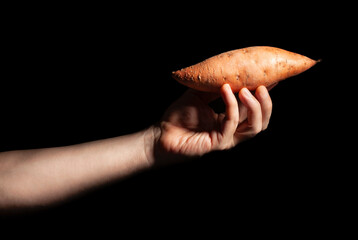 sweet potato in hand on black background