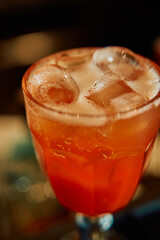 Refreshing orange cocktail in glass with ice cubes on a dark background