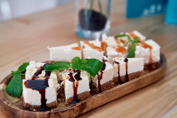 Delicious slices of cheesecake with mint and caramel drizzle on wooden plate