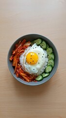 Delicious korean bibimbap with fried egg kimchi and cucumber on a wooden table