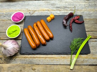 tender grilled sausages lie on a granite board next to peppers and herbs and bowls of spices