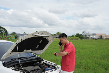 Depressed asian businessman is calling emergency help or car service center near broken car on road...