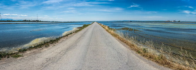 Asphalt road that disappears into infinity between two sheets of water