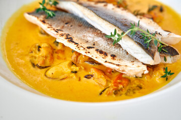 Grilled sea bass with mussels in saffron cream sauce garnished with thyme sprigs