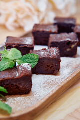 Decadent chocolate brownies with mint garnish on wooden tray, sugary dusting