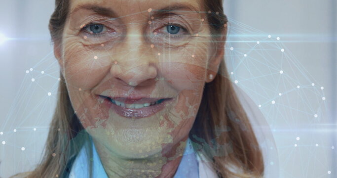 Displaying senior woman wearing white coat revealing glowing network overlay on face within office - Powered by Adobe