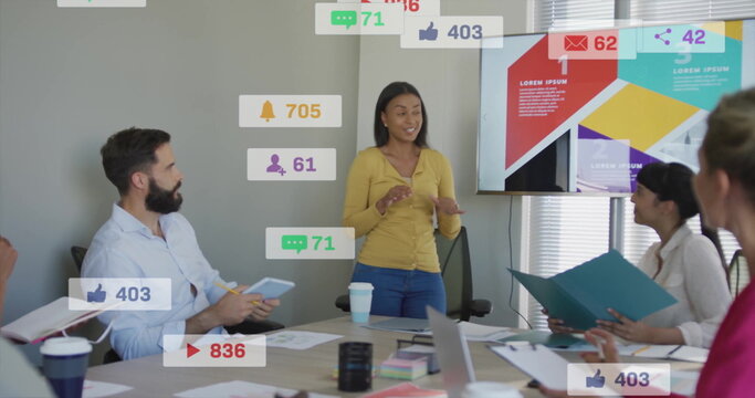 Woman in mustard cardigan presenting social media metrics on screen in meeting room with laptop