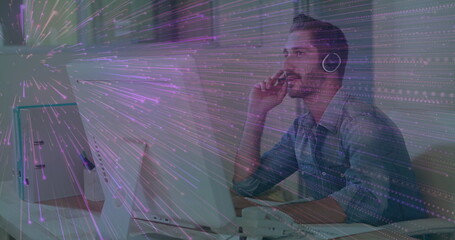 IT pro wearing blue shirt thinking in office with two monitors, keyboard, handset, mug, headphones