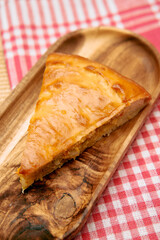 Golden slice of traditional cheese pie on wooden serving plate with red checkered tablecloth