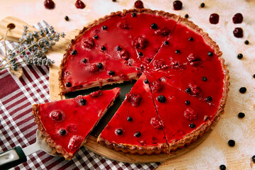 Delicious red berry tart with sliced piece surrounded by fresh berries and flowers on plaid...