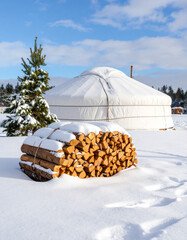 A stack of firewood tied with a rope beside a Mongolian ger in a snowy winter landscape.