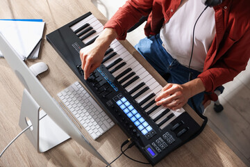 Man working with MIDI keyboard at wooden table indoors, above view