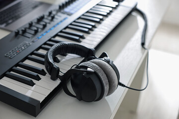 MIDI keyboard with headphones on white wooden table indoors, closeup