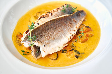 Grilled sea bass fillet with fresh thyme in creamy mussel saffron sauce garnished with herbs