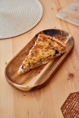 Savory quiche slice on wooden platter: homemade, rustic, tasty pastry displayed on table setting