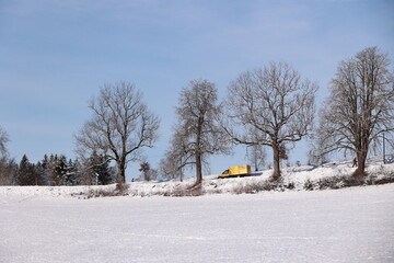 A yellow truck is driving down a snowy road in a field