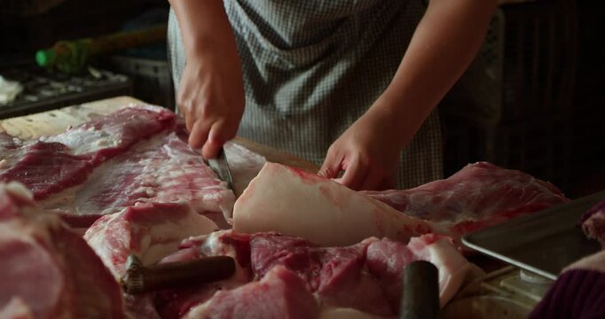 Hanoi, Vietnam - July 17, 2024: A pork vendor cuts raw meat. The picture shows a typical meat preparation process at a local market: cutting pork into parts for sale.