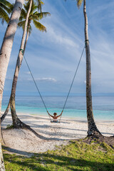 Woman on tropical beach swing and enjoying the ocean view and freedom under palm trees, perfect...