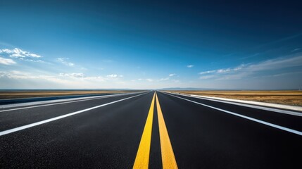 Fototapeta premium Wide empty highway with double yellow lines extending towards horizon under blue sky with clouds
