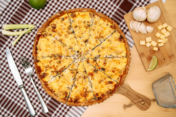 Mushroom cheese quiche on checkered tablecloth with ingredients and cutlery
