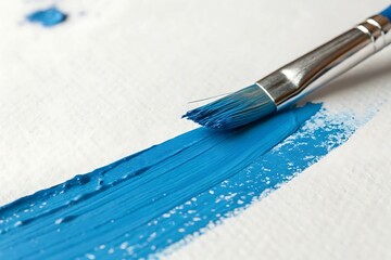 Close up of a paintbrush applying a stroke of vibrant blue paint on a white background.