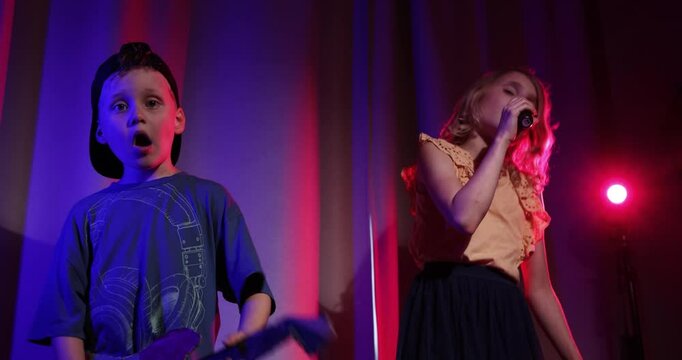children singing performance at home. boy playing cardboard guitar and girl sing in microphone in neon lights. music band