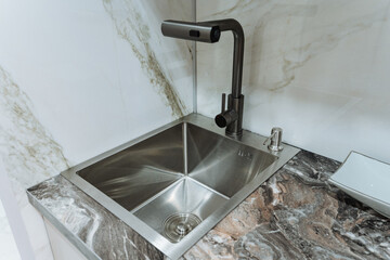 A modern stainless steel sink outfitted with an elegant black faucet is elegantly placed on a...