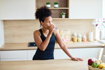 Portrait of a happy young woman holding a glass and drinking water and having a healthy breakfast...