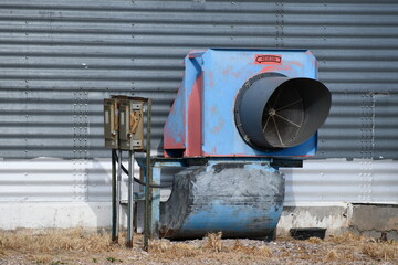 Large industrial vent fan on side of grain silo. Manual shutoff switch attached. Rotation direction sign on fan. © Trevor Cook
