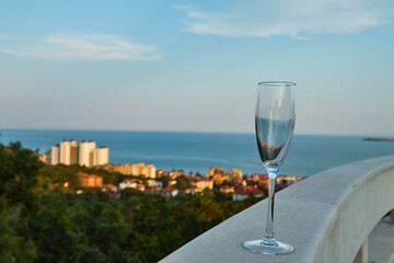 Empty glass of champagne on railing of a restaurant against the backdrop of sea at sunset. Concept of romance, summer, relaxation, romantic evening