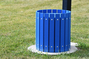 Blue wooden trash can. Bottom portion of doggie poo station. Cement base in grass field.