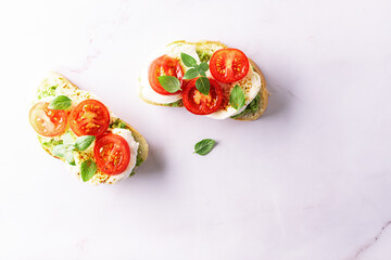 Fresh homemade caprese sandwich with avocado paste, mozzarella cheese, cherry tomatoes, fresh aromatic basil leaves and spicy hot oil top view. Healthy homemade food concept.