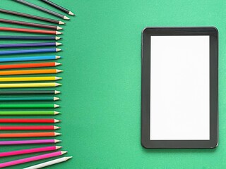 A textured green background with a blank tablet in the center. Colorful pencils arranged on the...