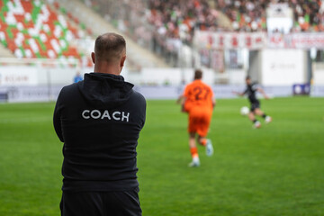 Head coach's back and soccer match at the stadium in the background.