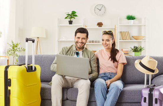 Couple tourists booking hotel online via laptop computer, planning vacation trip, posing on comfortable sofa with packed suitcases, going to have holidays in summer. Traveling concept - Powered by Adobe