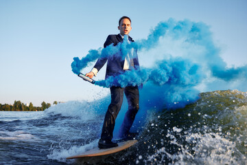 Professional businessman wake-surfing with vibrant blue smoke on a sunny day
