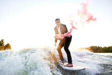 Man Surfing On A Wave Dressed In A Suit Holding Smoke Flare