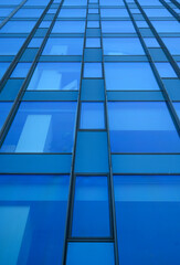 Close-up of modern glass skyscraper facade with reflective blue panels emphasizing strong vertical...