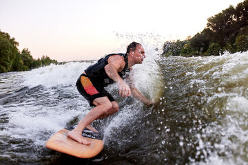 Man riding a surfboard on river wave with sunset light