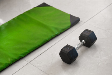 Dumbbell and green exercise mat on tiled floor in home workout setup