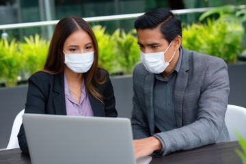 Masked professionals collaborating on laptop