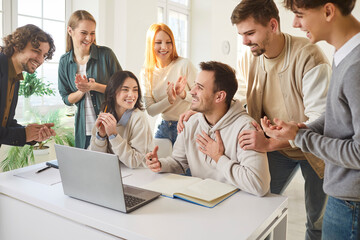 Group of happy smiling young college or university students sitting at the desk in the classroom with laptop rejoicing at successful educational project. Education and knowledge concept.